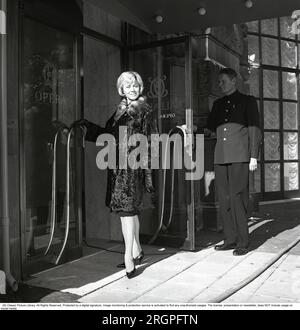 Service in den 1960er. Eine junge, modische Frau steht vor der Tür des Restaurants Operakällaren in Stockholm, mit einem Portier, der die Tür galant hochhält. Schweden 1962. Kristoffersson Ref. CV87-6 Stockfoto