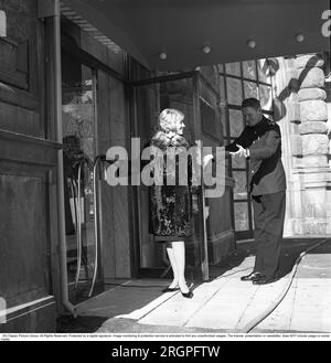 Service in den 1960er. Eine junge, modische Frau steht vor der Tür des Restaurants Operakällaren in Stockholm, mit einem Portier, der die Tür galant hochhält. Schweden 1962. Kristoffersson Ref. CV87-4 Stockfoto