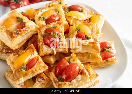 Blättern Sie mit Gebäck-Snacks mit Tomaten, Frischkäse und Kräuterpesto, Fingerfood auf einem weißen Teller für ein kaltes Party-Buffet, ausgewählter Fokus, enge Tiefe des Torten Stockfoto
