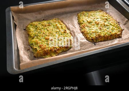 Gebackener Teig aus Zucchini und Haferflocken als Basis für vegane kohlenhydratarme Pizza oder Gemüsekuchen auf einem Tablett mit Backpapier, dunklem Hintergrund, Kopierbereich, Stockfoto