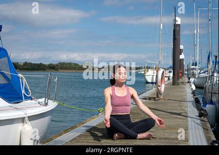 Eine Frau, die Yoga macht und auf einem Ponton meditiert. Yachtleben Stockfoto