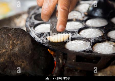 Frau bereitet Kokosnuss-thai-Desserts zu. Kanom krok ist ein leckeres thailändisches Mini-Pfannkuchen auf Kokosnussmilchbasis, das ebenfalls beliebt ist. Stockfoto