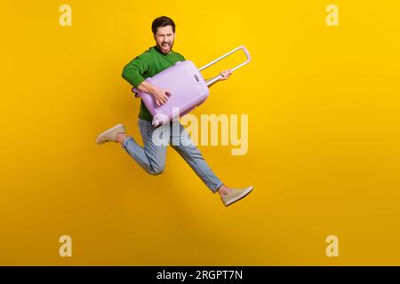 Ganzkörperfoto eines verrückten, schreienden jungen Gitarristen, der seinen Koffer in der Hand hält und isoliert auf gelbem Hintergrund singt Stockfoto