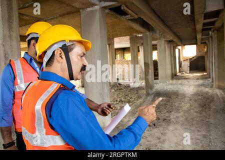 Zwei indische Bauingenieurinnen oder Architekten mit Helm und Weste, die auf der Baustelle, Immobilien, arbeiten. Stockfoto