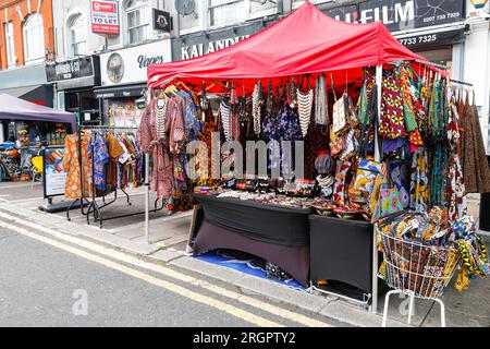 Verkaufsstände mit Kleidung und Souvenirs aus den afrikanischen und afro-karibischen Ländern, Brixton Station Road Market, Brixton, South London, England Stockfoto