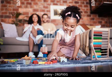 Kind, Spielzeug und Spielen zu Hause mit Entwicklungs- und Bausteinen im Wohnzimmer. Familie, Spaß und Jugend lernen mit einem jungen Mädchen und Eltern in einem Stockfoto