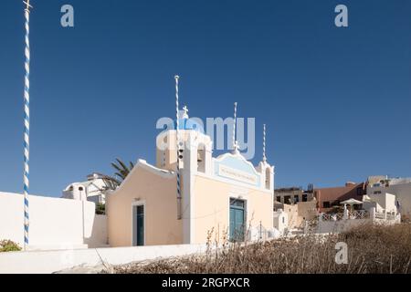 Foto der Heiligen Dimitrios Oia Heilig-orthodoxe Kirche, eine kleine pfirsichfarbene Kirche mit einer blauen Kuppel, mit blau-weißen Stangen um den Kopf herum und klar Stockfoto