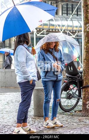 Zwei Frauen, die sich unter Regenschirmen im regnerischen Paris in Frankreich verstecken. Stockfoto