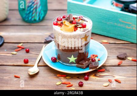 Chiapudding mit Schokolade, frischen Cranberrys, Mandeln, gehackten Schokoriegeln, Kürbiskernen und Goji-Beeren auf rustikalem Hintergrund Stockfoto