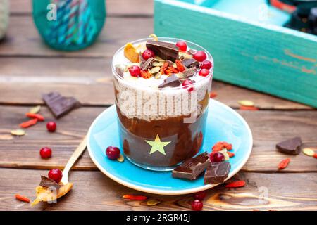 Chiapudding mit Schokolade, frischen Cranberrys, Mandeln, gehackten Schokoriegeln, Kürbiskernen und Goji-Beeren auf rustikalem Hintergrund Stockfoto