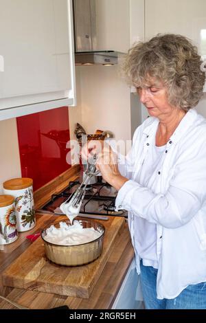 Frau zu Hause kocht Eiweiß mit der Hand zu steifen Gipfeln, um einen Schokoladenmousse oder Baiser zu machen Stockfoto