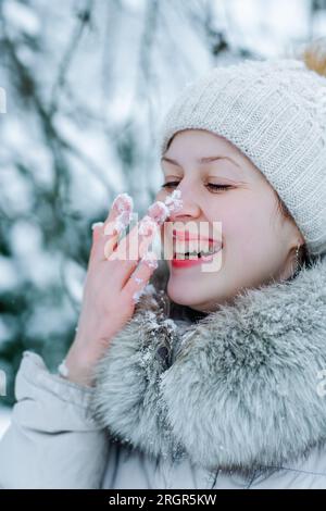 Porträt einer jungen glücklichen Frau in warmer Winterkleidung mit Schnee auf der Nase Stockfoto