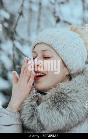 Porträt einer jungen glücklichen Frau in warmer Winterkleidung mit Schnee auf der Nase Stockfoto