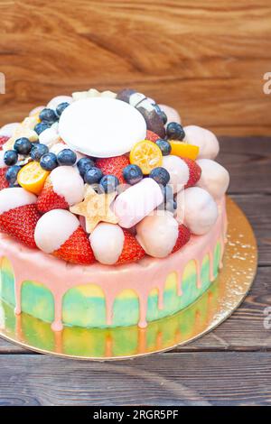 Farbenfroher Kuchen mit Erdbeeren in geschmolzener weißer Schokolade, mit rosafarbener Glasur, frischen Himbeeren, Heidelbeeren und Kumquat Stockfoto
