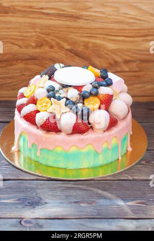Farbenfroher Kuchen mit Erdbeeren in geschmolzener weißer Schokolade, mit rosafarbener Glasur, frischen Himbeeren, Heidelbeeren und Kumquat Stockfoto