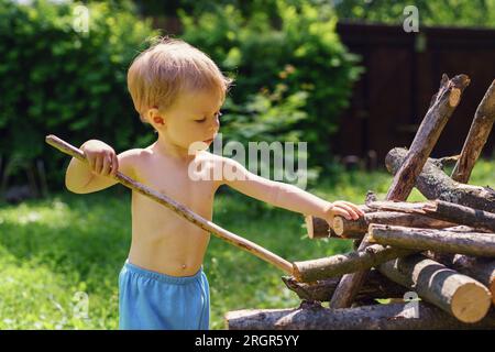 Der kleine Junge stapelt im Garten Stämme auf einem Haufen Stockfoto