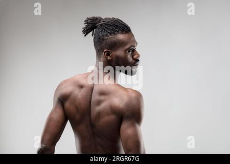 Ein muskulöser Mann dreht sich zur Seite und zeigt attraktive Rückenmuskeln. Es ist nicht Glück, sondern hartes Training, das seinen Körper begehrenswert macht. Dunkelbraune Haut, pur Stockfoto