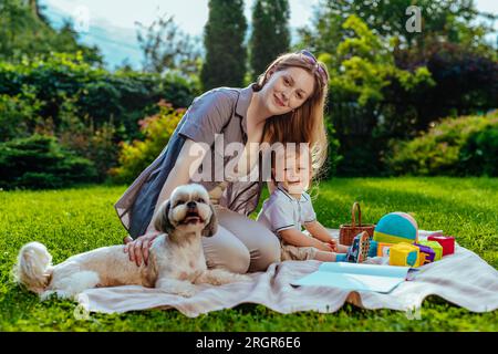 Junge Mutter mit einjährigem Kind und Hund, die im Sommer im Park sitzen Stockfoto