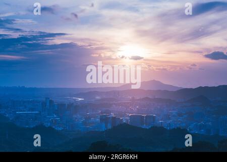Blauer Himmel mit weißen dynamischen Wolken über der Stadt bei Sonnenuntergang. Blick auf die städtische Landschaft vom Berg Dajianshan, New Taipei City, Taiwan Stockfoto