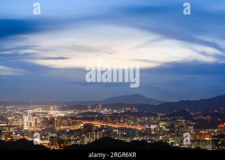 Blauer Himmel mit weißen dynamischen Wolken über der Stadt bei Sonnenuntergang. Blick auf die städtische Landschaft vom Berg Dajianshan, New Taipei City, Taiwan Stockfoto