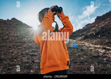 Porträt eines Tourismusjungen, der in einem Fernglas in den Bergen sucht Stockfoto