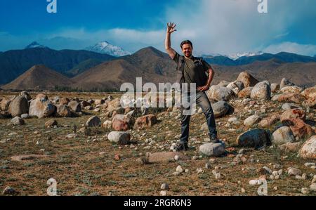 Ein junger lächelnder Mann steht auf dem Berg und winkt mit der Hand Stockfoto