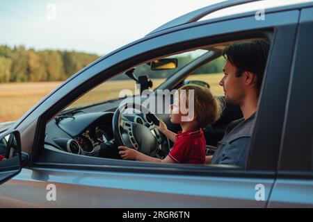Vater mit seinem zweijährigen Sohn, der Auto auf einem Feld fährt Stockfoto