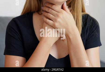 Halsschmerzen. Nahaufnahme einer schönen Frau mit Händen am Hals. Konzept von Halsschmerzen, Pharyngitis, Laryngitis, Thyreoiditis, Ersticken oder Dysphagie. Stockfoto