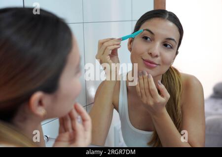 Gesichtshaarentfernung. Nahaufnahme einer schönen jungen Frau, die sich zu Hause mit einem Rasierer rasiert. Stockfoto