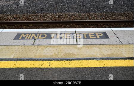 Schild „Achtung der Stufe“ am Bahnsteig am Bahnhof Torquay, gelbe Linie und taktile Pflaster. Stockfoto