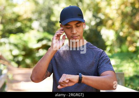 Attraktiver asiatischer Mann synchronisiert Fitnessgerät mit Ohrhörern, läuft im grünen Park Stockfoto