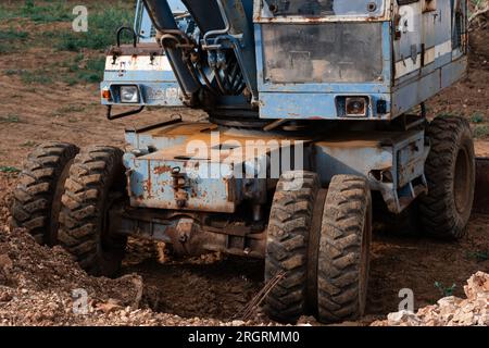 Ein alter rostig blauer Bagger steht auf einer Baustelle. Der rostige Löffel eines alten Hydraulikbaggers wird auf den Boden abgesenkt. Stockfoto