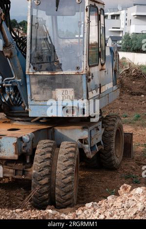 Ein alter rostig blauer Bagger steht auf einer Baustelle. Der rostige Löffel eines alten Hydraulikbaggers wird auf den Boden abgesenkt. Stockfoto