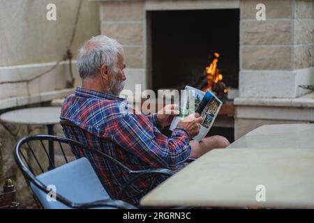 Ein alter Mann in einem karierten Hemd sitzt am Tisch und liest Zeitung. Ein alter Bauer und Fischer ruht in seiner eigenen Villa. Stockfoto