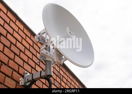 Weiße Satellitenschüssel vor brauner Backsteinwand Stockfoto