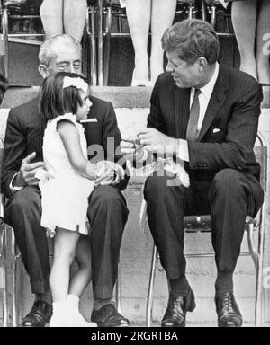 Mexiko-Stadt, Mexiko: 30. Juni 1962 Präsident Kennedy dankt einem kleinen mexikanischen Mädchen, das ihm heute bei einer Feier zum 4. Juli für die amerikanische Kolonie in Mexiko-Stadt einen Blumenstrauß schenkte. Bei dem Mädchen ist Gustavo Bas, Gouverneur des Staates Mexiko. Stockfoto