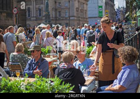 Royal Mile, Schottland, Großbritannien. 11. August 2023. Straßenkünstler auf der High Street finden die windigen Bedingungen schwierig, aber heißes Wetter mit Temperaturen von etwas über 20 Grad willkommen. Später am Tag kommen Menschenmassen mit mehreren anderen Darbietungen im Stadtzentrum an. Abbildung: Die Gäste genießen ein Getränk im Freien in einem der Cafés im hohen Stree. Kredit: Archwhite/alamy Live News. Stockfoto