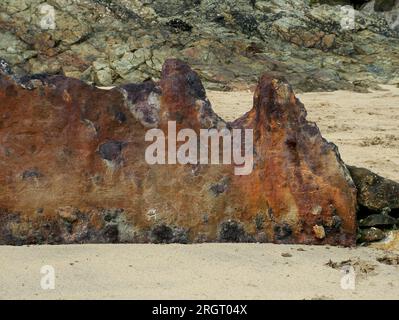 Herbstsonne auf den kontrastierenden Farben der Felsen und den rostenden alten Stahlplatten eines Schiffes an einem Strand in Cornwall. Stockfoto