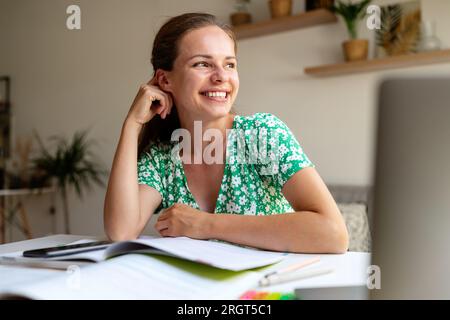 Portrait glücklicher junger Erwachsener sitzt zu Hause am Schreibtisch und macht Hausaufgaben und lächelt. Stockfoto