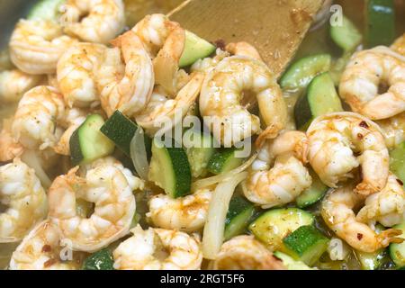 Nahaufnahme von Garnelen mit Zucchini, Zwiebeln, Öl und Gewürzen, Kochen in einer Pfanne. Stockfoto