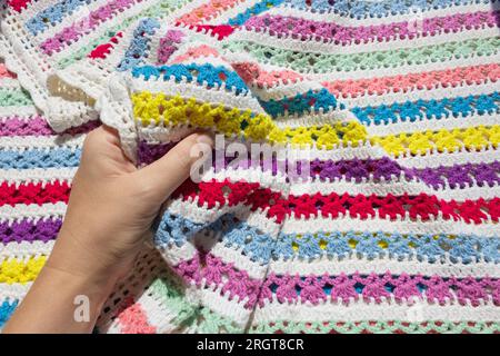 Eine Hand, die eine weiche Strickdecke im hellen Licht der Sonne berührt. Stockfoto