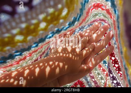 Die Hand eines Kindes in der Hand der Mutter unter einer Decke in hellem Sonnenlicht. Stockfoto