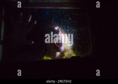 Gruselige Frau hinter dem Fenster in der Nacht Halloween Horror Hintergrund Stockfoto