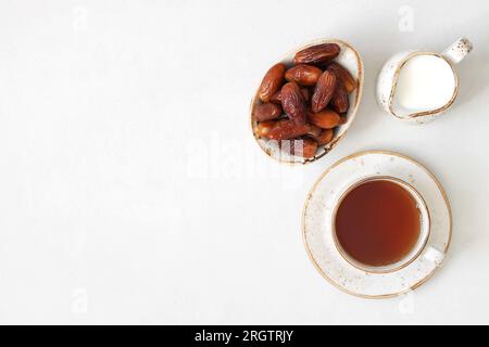 Eine Tasse Tee, getrocknete Datteln und ein Milchkännchen auf weißem Hintergrund. Natürliches, gesundes Frühstück. Kopierbereich, Draufsicht, flach liegend. Stockfoto