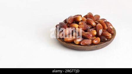 Köstliche getrocknete Datteln auf einem Holzteller auf weißem Hintergrund. Natürliche orientalische Süßigkeiten. Speicherplatz kopieren. Stockfoto