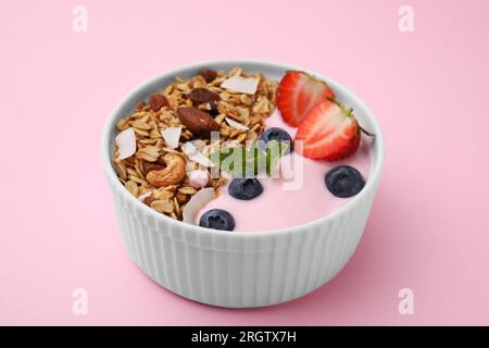 Leckeres Müsli, Joghurt und frische Beeren in der Schüssel auf pinkfarbenem Hintergrund, Nahaufnahme. Gesundes Frühstück Stockfoto