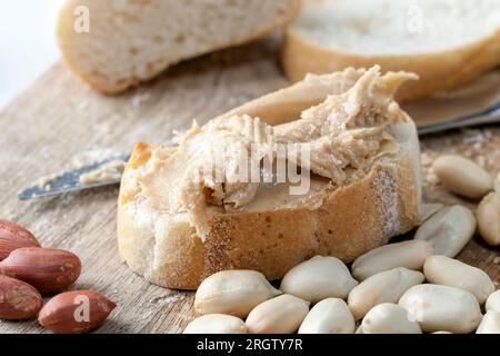 Zutaten für die Zubereitung eines schnellen Frühstücks mit Brot und Erdnüssen, Erdnusspaste geröstete Erdnüsse, köstliche Erdnussbutter und Weißbrot auf dem Tisch Stockfoto