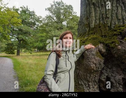 Porträt einer lächelnden Frau, die sich im Wald auf den Baumstamm lehnt Stockfoto