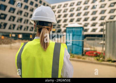 Rückansicht einer Bauarbeiterin im Schutzhelm vor dem Bauhintergrund Stockfoto