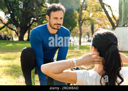 Männlicher Trainer hilft jungen Frauen beim Sport im Park. Stockfoto